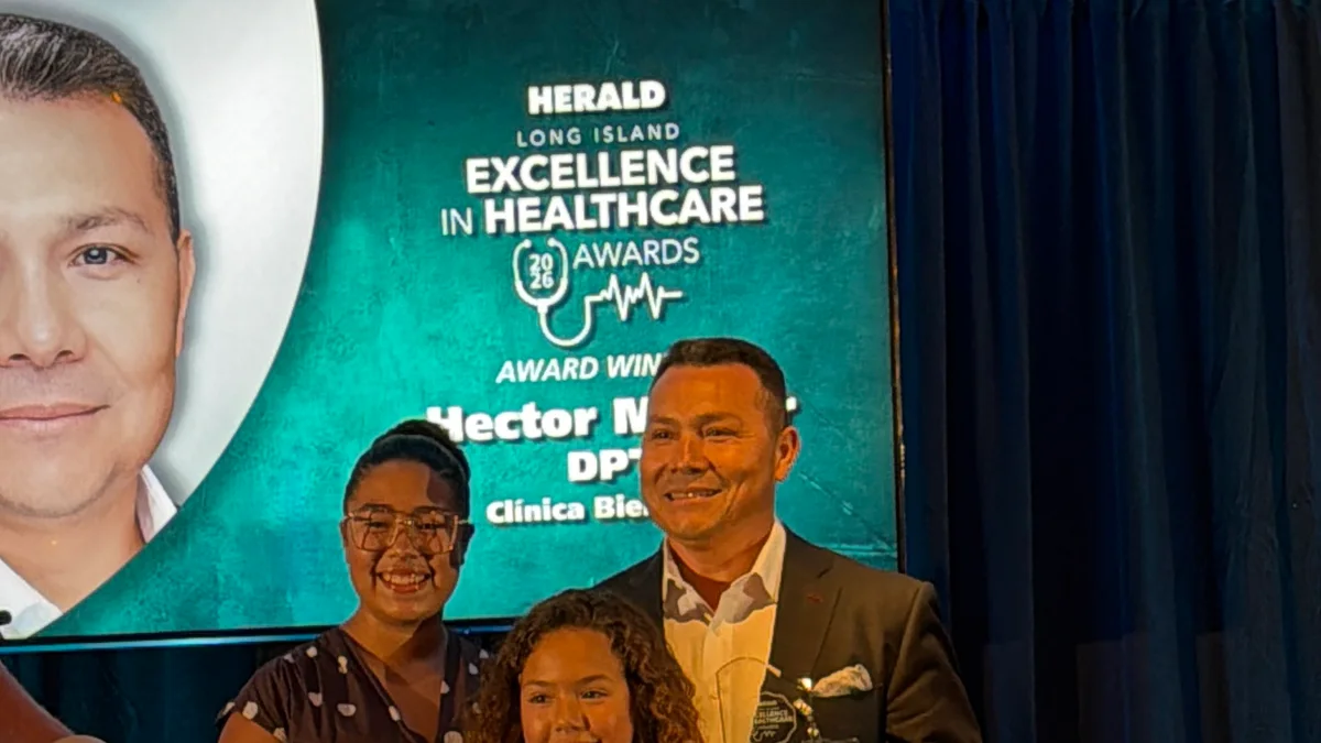 Hector Melgar, DPT, en el escenario de los HERALD Long Island Excellence in Healthcare Awards 2026, con su nombre proyectado como ganador