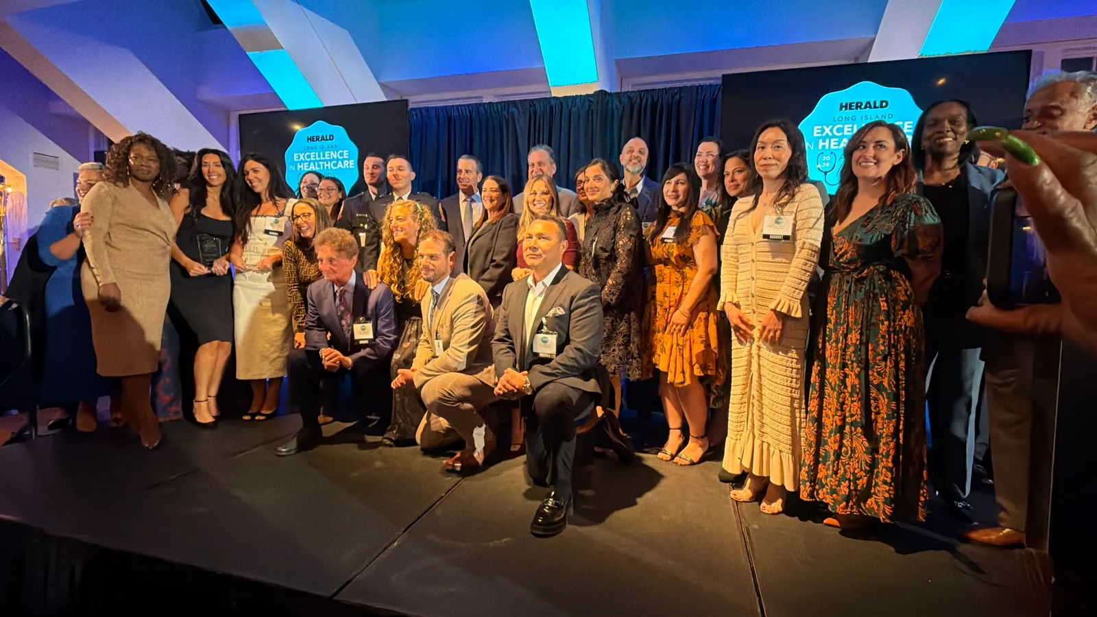Los homenajeados de los HERALD Long Island Excellence in Healthcare Awards 2026 en el escenario; Hector Melgar, DPT, de Clínica Bienestar, arrodillado en la primera fila